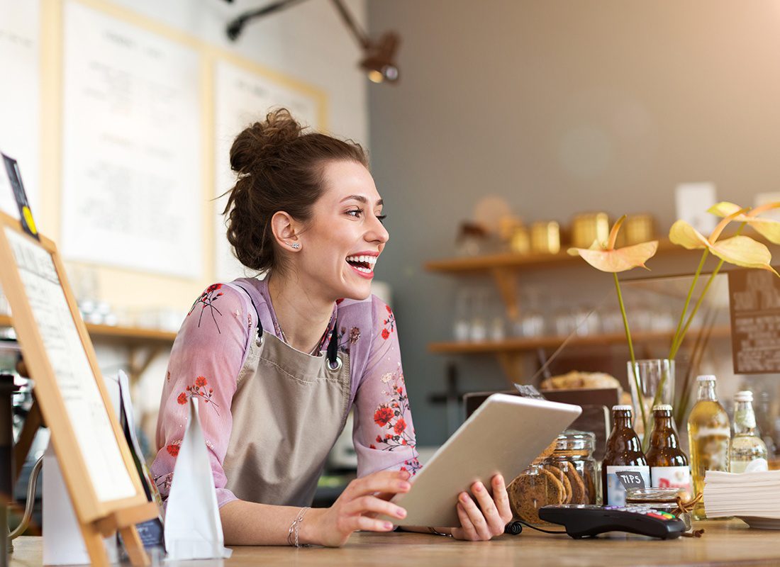 Business Insurance - Happy Business Owner Holds a Tablet and Smiles at Her Cafe